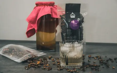 Napój z cascary, czyli co to jest kombucha z kawy, w szklance z lodem i słomką. Obok słoik z napojem i paczka z cascara.