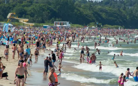 Tłumy ludzi na plaży i w wodzie, zjeżdżalnie wodne w tle. Idealne miejsce na wakacje w Polsce!