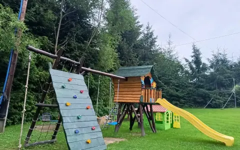 Kolorowy plac zabaw w Polańczyku: ścianka wspinaczkowa, domek ze zjeżdżalnią i huśtawki. Idealne polańczyk atrakcje dla dzieci.