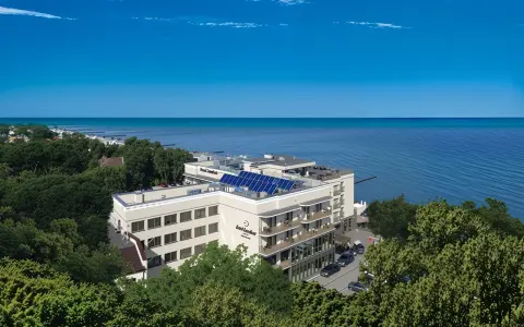 Nowoczesny hotel z panelami słonecznymi nad polskim morzem, otoczony zielenią.