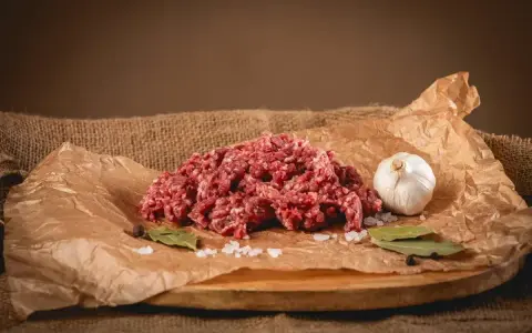 Surowe mielone mięso, idealne na soczyste burgery. Obok czosnek, liście laurowe i sól.
