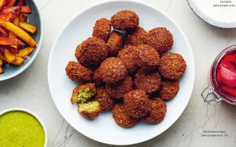 Talerz pełen chrupiących kuleczek, które są idealnym przykładem tego, co to jest falafel. Podane z zielonym sosem i frytkami.