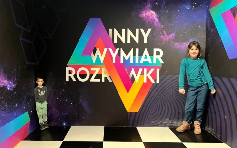 Dzieci w "Innym Wymiarze Rozrywki" w Warszawie. Kolorowa ściana z motywem kosmosu i geometrycznymi kształtami.