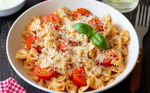 Pyszny makaron farfalle z pomidorkami koktajlowymi i parmezanem, idealny na kolację.