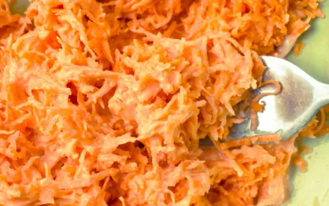 Pyszna surówka z marchewki jak z restauracji, kremowa i apetyczna. Widoczna łyżka widelca zagłębiająca się w jej wnętrze.