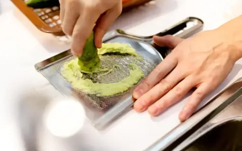 Ręka trze korzeń wasabi o tarkę. To właśnie tak powstaje świeże wasabi, które dodaje ostrości potrawom.