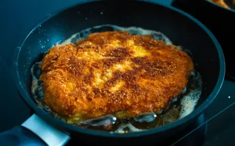 Złocisty kotlet schabowy smaży się na patelni. Idealnie chrupiąca panierka i bulgoczący tłuszcz świadczą o tym, jak długo smażyć schabowe, by były perfekcyjne.