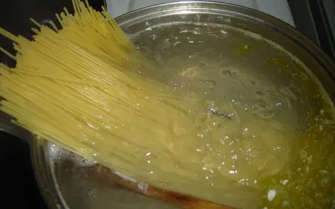 Długi makaron spaghetti zanurza się w gotującej wodzie. Czas, ile gotuje się makaron, zależy od jego grubości.