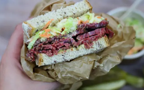 Pyszna kanapka z pastrami, z chrupiącą surówką i musztardą, zawinięta w papier.