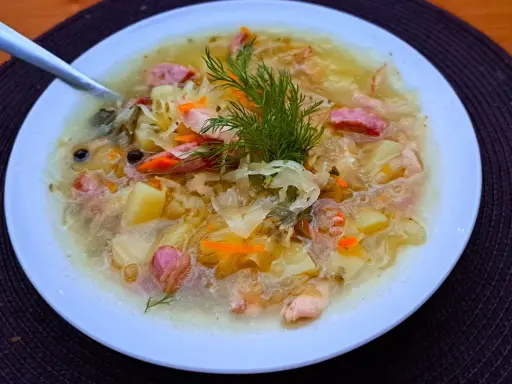 Syta zupa z kiszonej kapusty z ziemniakami i kiełbasą, ozdobiona koperkiem. Pyszne dania z kapusty na zimowe wieczory.