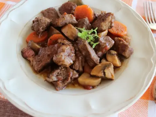 Bœuf bourguignon: duszona wołowina z marchewką i pieczarkami, podana na talerzu.