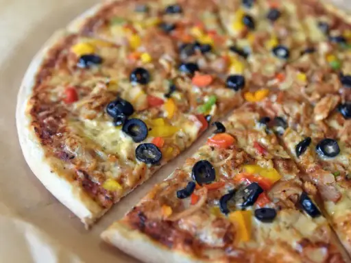 Pyszna pizza sycylijska z oliwkami, papryką i serem, pokrojona na kawałki.