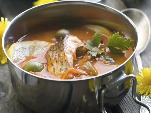 Aromaticzna rosyjska zupa rybna z kawałkami ryby, oliwkami, cytryną i natką pietruszki w metalowej misce.