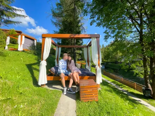 Idealne miejsce, gdzie na weekend we dwoje. Para odpoczywa na łóżku pod baldachimem w otoczeniu zieleni.