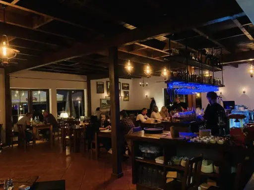 Wnętrze restauracji z ludźmi przy stołach i barem.