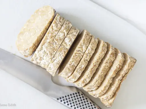 Pokrojony w plastry tempeh, czyli fermentowana soja, leży obok noża. To świetny składnik do wegańskich potraw.