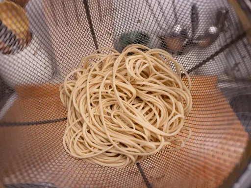 Kłębek jasnego makaronu alkalicznego w metalowym sicie.