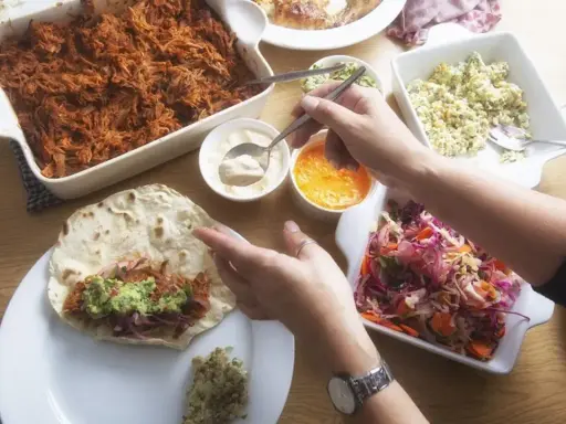 Stół z potrawami do burrito: szarpana wieprzowina, surówka, guacamole i sosy.