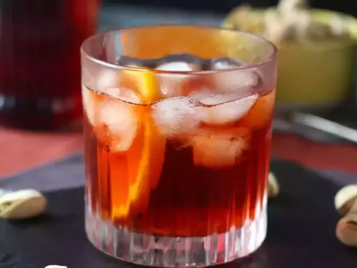 Orzeźwiający negroni sbagliato z lodem i plasterkiem pomarańczy, podany z pistacjami.