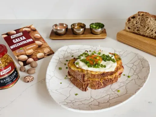 Pyszny croque madame z jajkiem sadzonym i szczypiorkiem, obok musztarda francuska i gałka muszkatołowa.