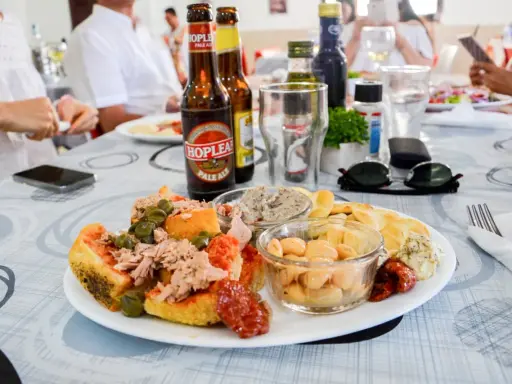 Malta jedzenie: talerz z tuńczykiem, kaparami, fasolą i pieczywem, obok piwo i okulary przeciwsłoneczne.
