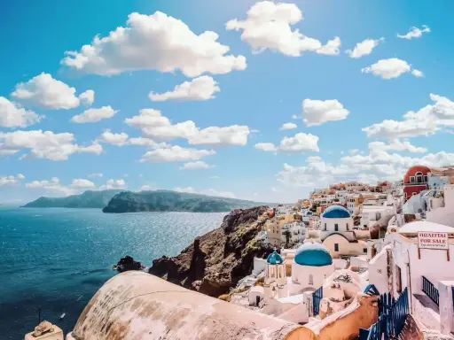 Santorini, Grecja. Białe domy z niebieskimi kopułami kościołów na zboczu góry, widok na morze. Zastanawiasz się, ile się leci do Grecji?