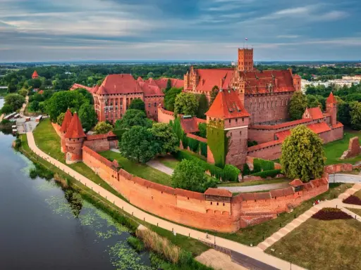 Potężny zamek w Malborku, największy zamek na świecie, otoczony murami obronnymi i rzeką, z czerwonymi dachami i wieżami.
