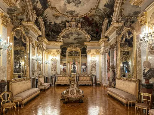 Złocone wnętrze muzeum w Madrycie, z malowanym sufitem, lustrami i antycznymi meblami.