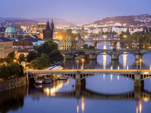 Praga nocą, z licznymi mostami na Wełtawie i oświetlonymi budynkami. Ciekawe ciekawostki o Czechach czekają na odkrycie w tym magicznym mieście.