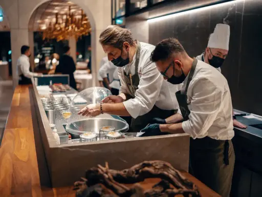 Szefowie kuchni w atelier amaro przygotowują dania. W tle widać eleganckie wnętrze restauracji.
