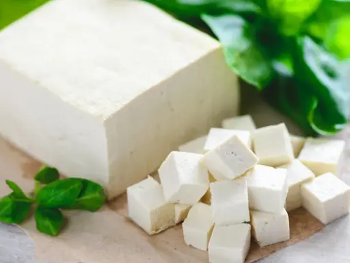 Kostka tofu i pokrojone w kostkę tofu na desce, ozdobione zielonymi liśćmi.