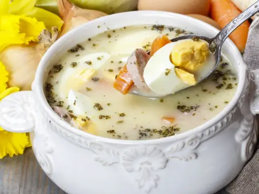 Aromaticzny żur z jajkiem i kiełbasą, podany w ozdobnej misce, z żółtymi narcyzami w tle.