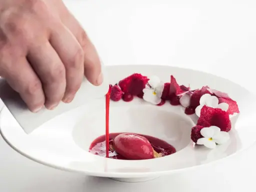 Wykwintny deser w restauracji z gwiazdką Michelin: malinowy sorbet z sosem i jadalnymi kwiatami, polany przez kucharza.