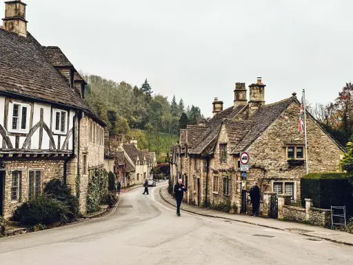 Kamienna uliczka w Cotswolds, z tradycyjnymi domami i drzewami na wzgórzach.