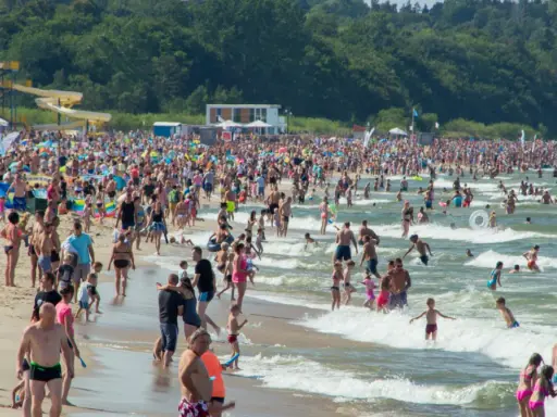 Tłumy ludzi na plaży i w wodzie, zjeżdżalnie wodne w tle. Idealne miejsce na wakacje w Polsce!
