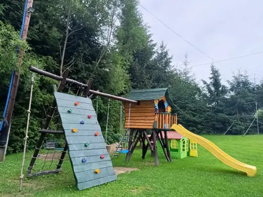 Kolorowy plac zabaw w Polańczyku: ścianka wspinaczkowa, domek ze zjeżdżalnią i huśtawki. Idealne polańczyk atrakcje dla dzieci.