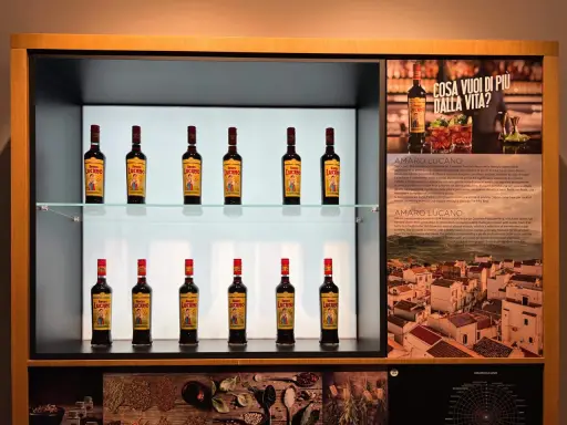 Butelki amaro Lucano stoją na półkach, tworząc elegancką ekspozycję.