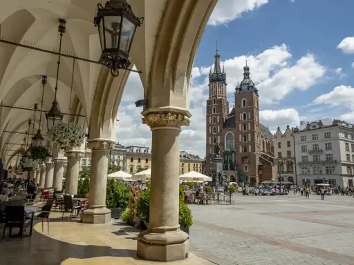 Urokliwe arkady Sukiennic w Krakowie, z widokiem na Kościół Mariacki i tętniący życiem Rynek. Stare miasto w Krakowie zachwyca.