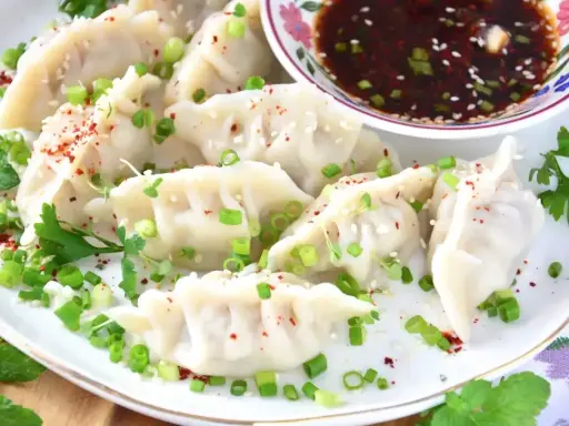 Pierożki gyoza, posypane szczypiorkiem i sezamem, podane z sosem.