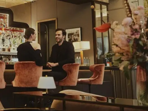 Para w eleganckim barze w Warszawie, uśmiechnięci, siedzą na aksamitnych stołkach. Idealna randka w stolicy.