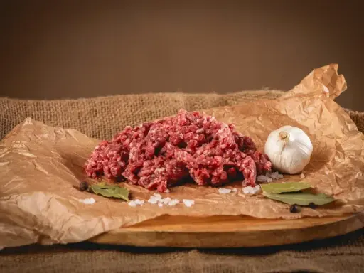 Surowe mielone mięso, idealne na soczyste burgery. Obok czosnek, liście laurowe i sól.