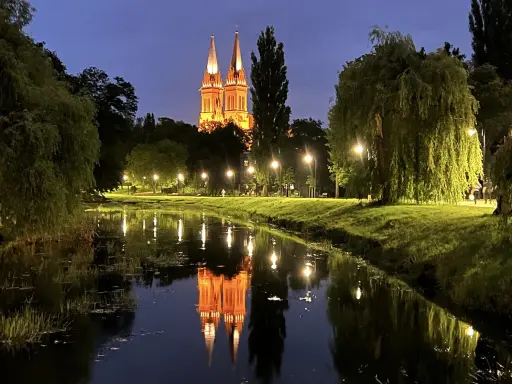 Wieczorny spacer nad rzeką we Włocławku. Podświetlona katedra odbija się w wodzie, tworząc magiczny widok. Idealne włocławek atrakcje na weekend.