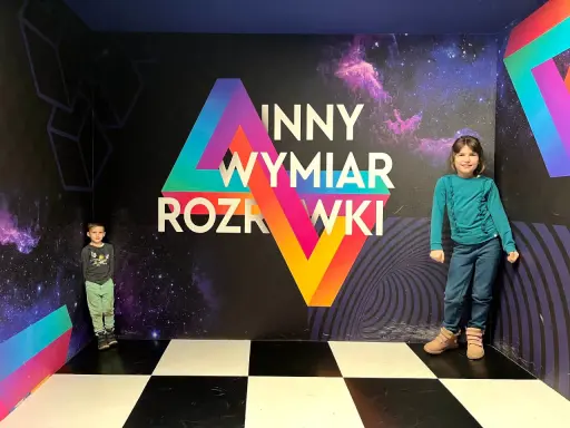 Dzieci w "Innym Wymiarze Rozrywki" w Warszawie. Kolorowa ściana z motywem kosmosu i geometrycznymi kształtami.