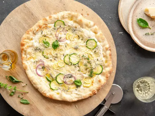 Pyszna pizza bianca z cukinią, cebulą i cytryną, podana na drewnianej desce.