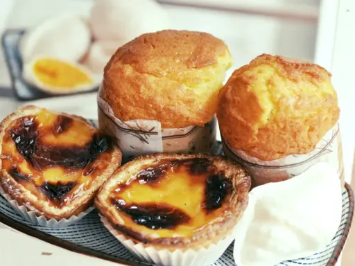 Pyszne portugalskie ciastka, w tym dwa kremowe pastel de nata i dwa muffinki, kuszą apetycznym wyglądem.