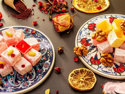 Kolorowe tureckie przysmaki, w tym lokum z pistacjami i orzechami, ozdobione suszonymi różami i plasterkami pomarańczy.