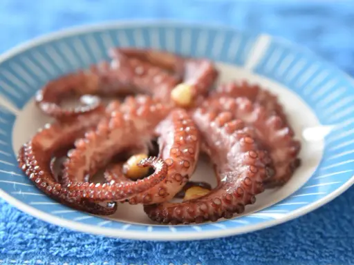 Gotowy ośmiornica przepis na talerzu z niebieskimi paskami. Delikatne macki z czosnkiem, idealne do degustacji.