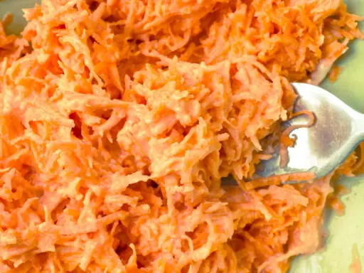 Pyszna surówka z marchewki jak z restauracji, kremowa i apetyczna. Widoczna łyżka widelca zagłębiająca się w jej wnętrze.