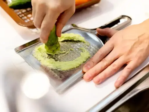 Ręka trze korzeń wasabi o tarkę. To właśnie tak powstaje świeże wasabi, które dodaje ostrości potrawom.