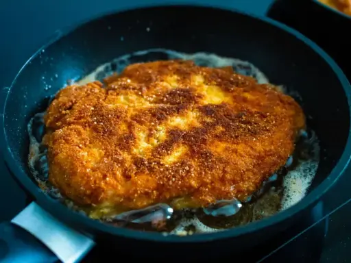 Złocisty kotlet schabowy smaży się na patelni. Idealnie chrupiąca panierka i bulgoczący tłuszcz świadczą o tym, jak długo smażyć schabowe, by były perfekcyjne.